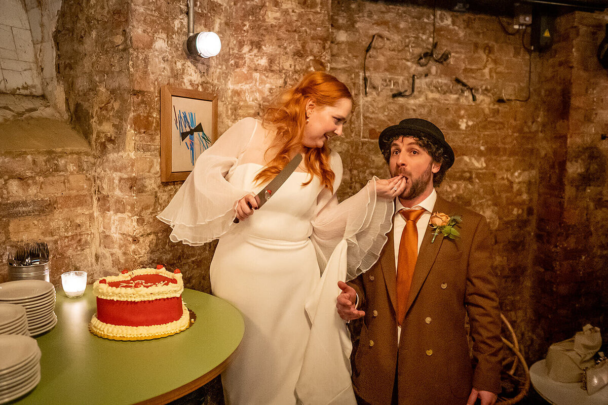 Hipster couple, bride feeding cake to groom at The Coin Laundry wedding Londno