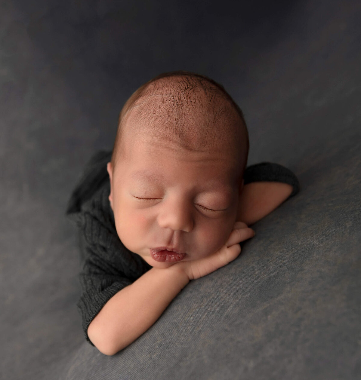 Newborn baby boy dressed in a grey romper posed chin on hands in an Erie Pa photography studio