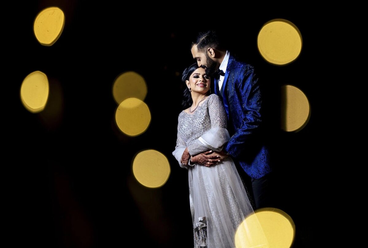 A couple in wedding attire lovingly embracing against a backdrop of golden bokeh lights, highlighting a romantic wedding moment.