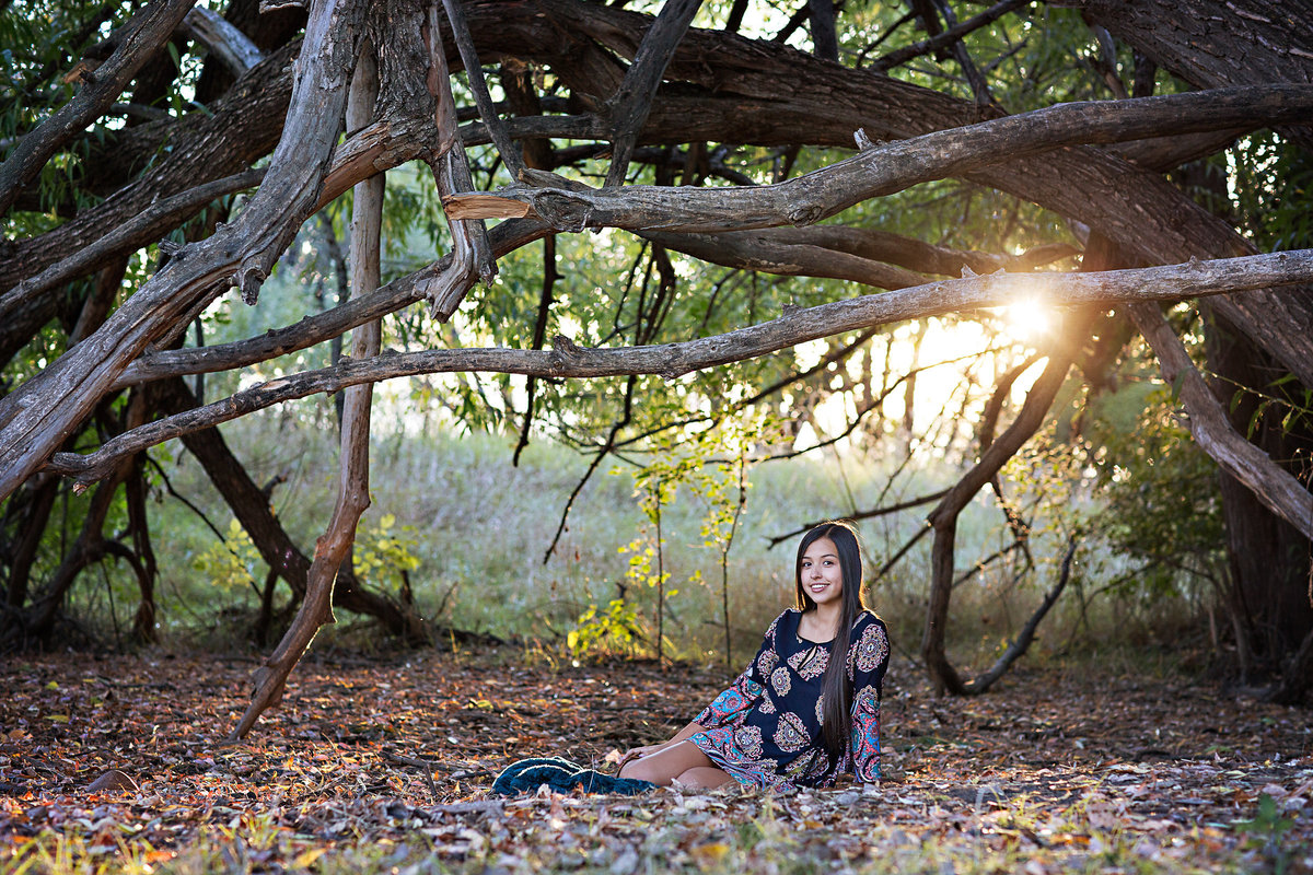 A senior girl sits among the trees in the fall leaves