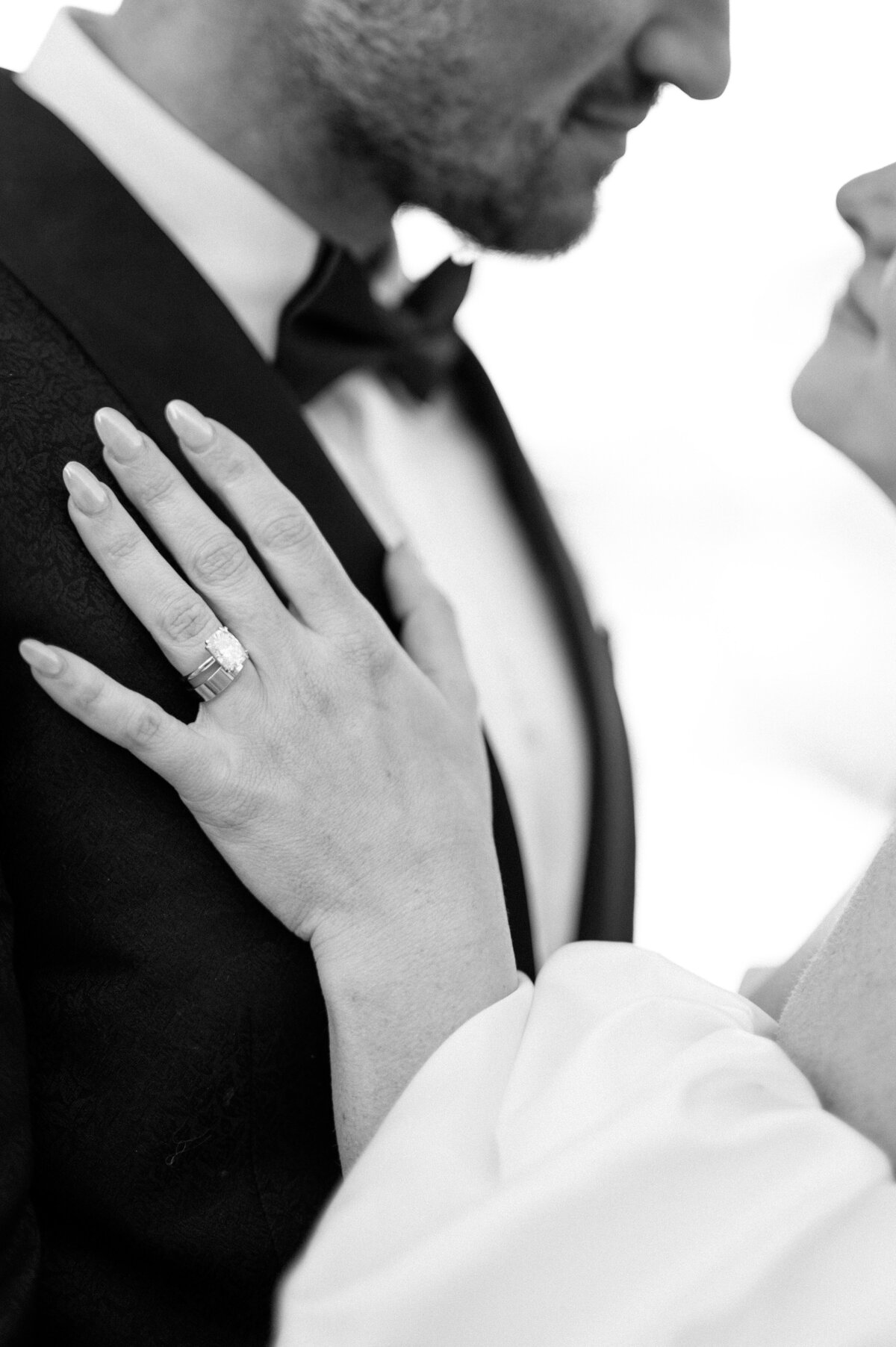Closeup of engagement ring as bride embraces groom