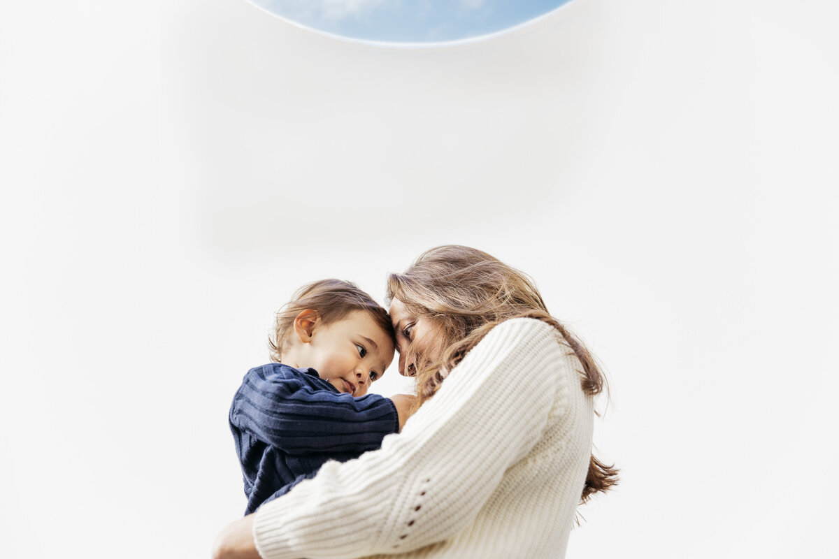 Mother is tenderly holding toddler son. 