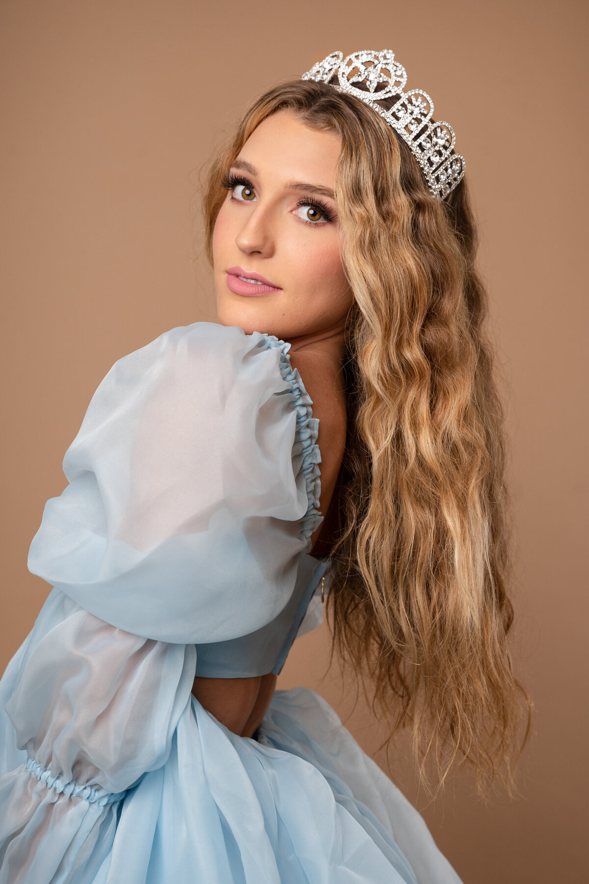 A woman with long blond hair wearing a tiara and a blue soft tulle dress