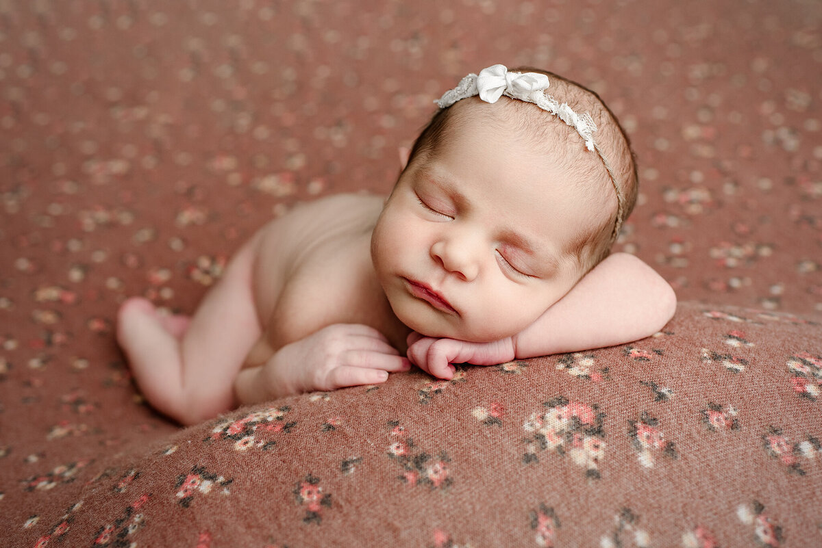 Newborn girl posed with head on hands on floral backdrop in St. Augustine, FL.