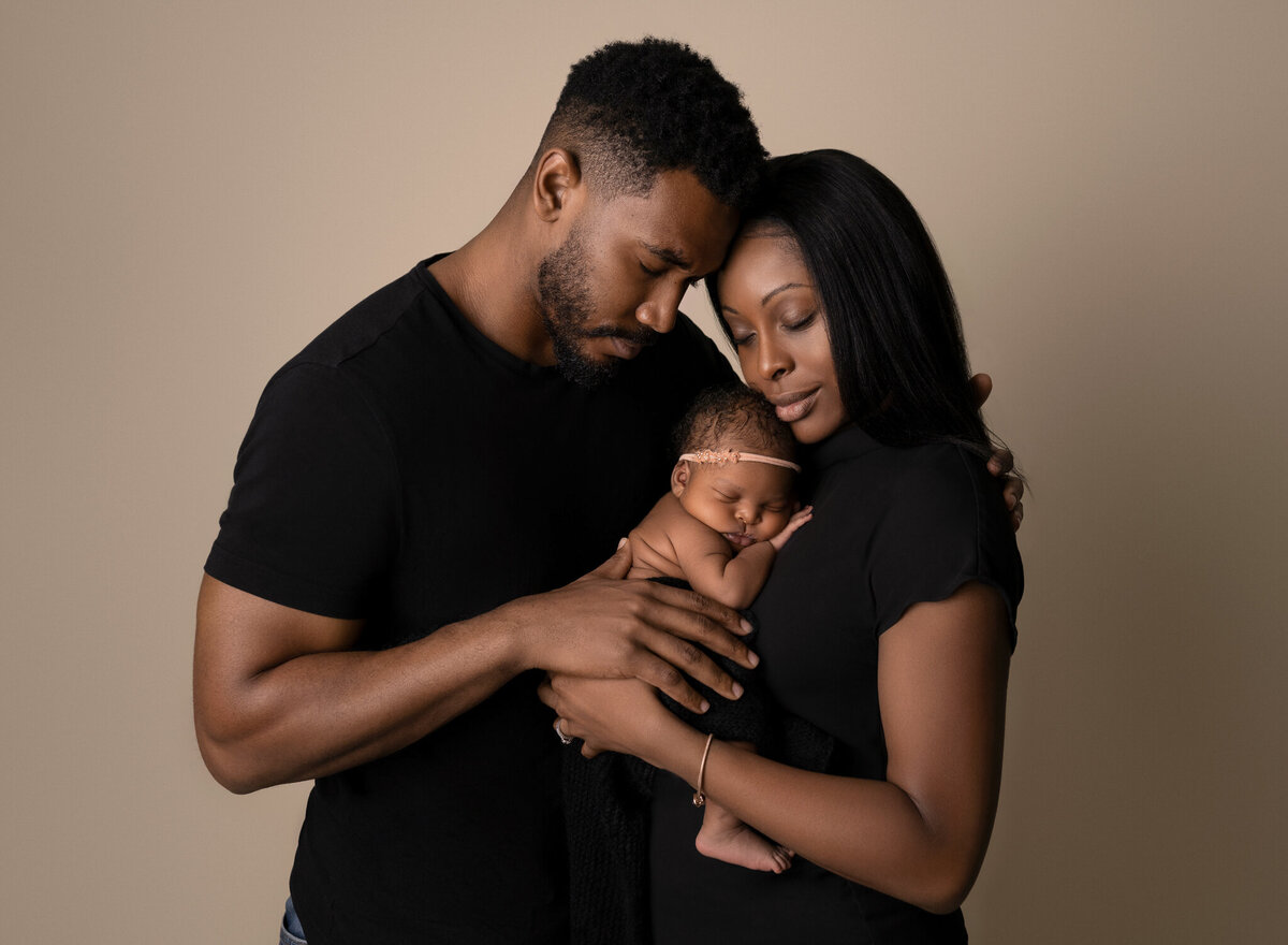 Newborn baby girl held by parents dressed in black against a soft beige studio backdrop | Austin and Leander newborn photographer