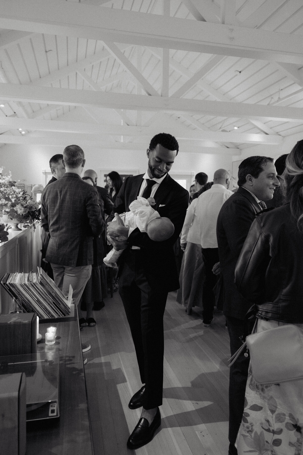 A heartfelt black and white wedding reception moment of a groom holding his baby while mingling with guests. We focus on capturing real, intimate moments that showcase love, connection, and the joy of a wedding day.