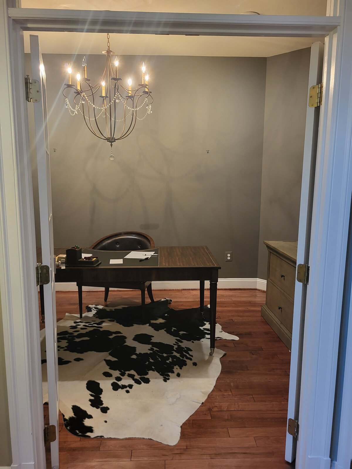 office with oversized light fixture with crystals, oversized desk with chair and file cabinet furniture piece and faux black and white rug