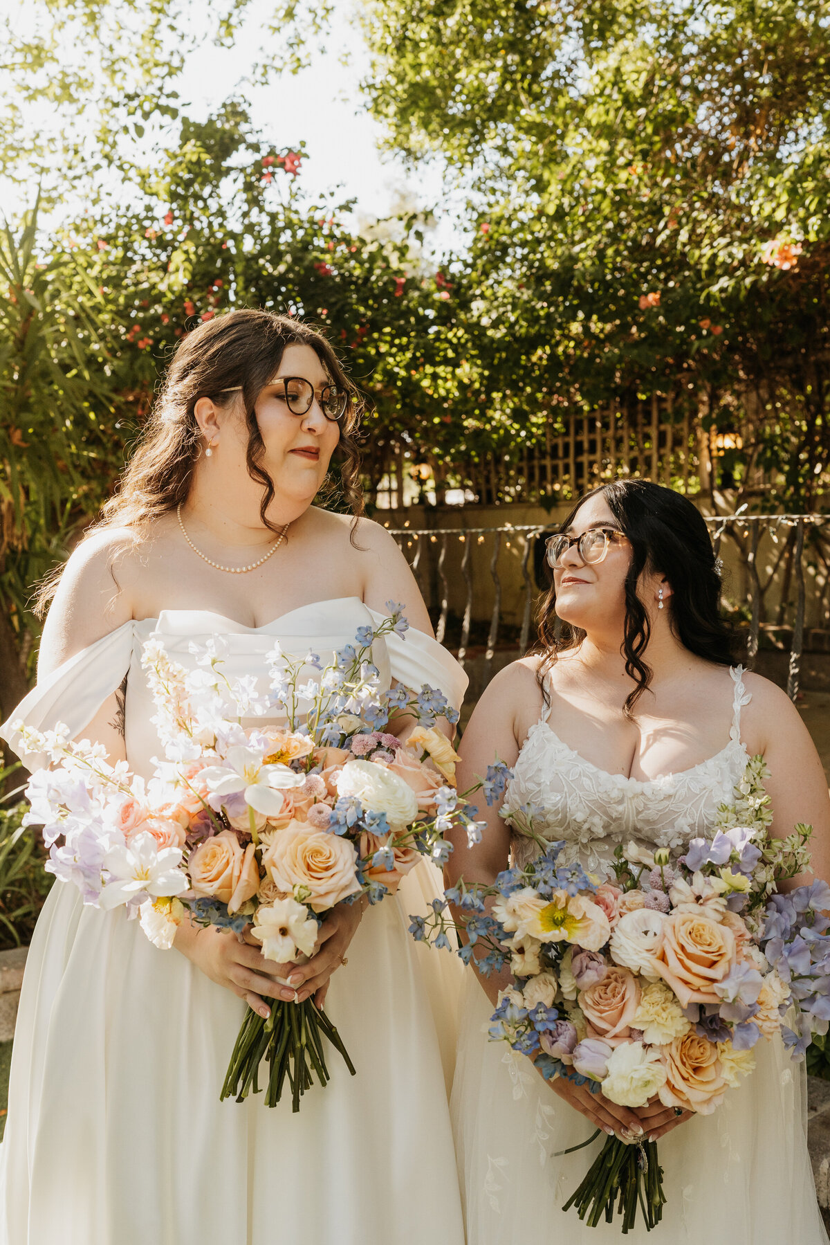 Two people in wedding dresses standing next to each other smiling at each other 