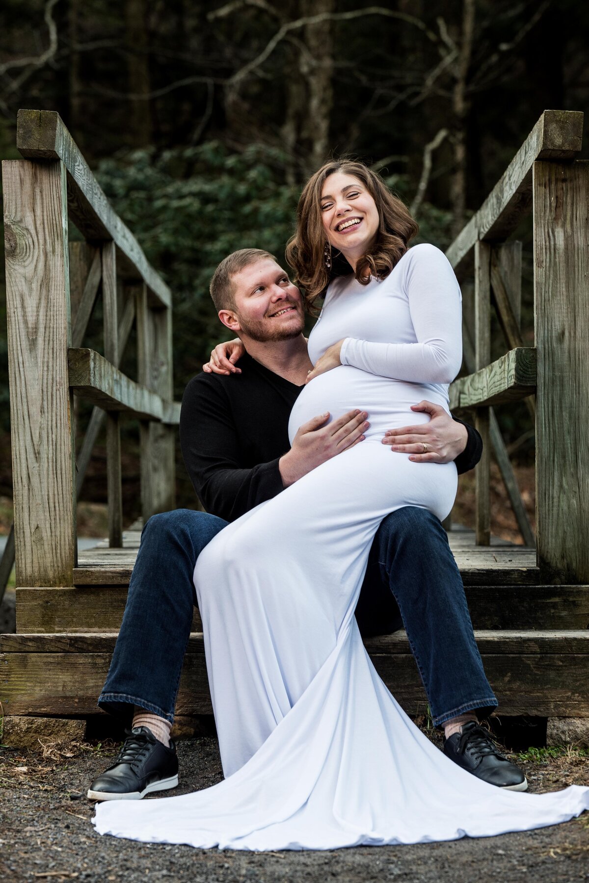 a pregnant woman sits on her husband's lap as he holds her baby bump