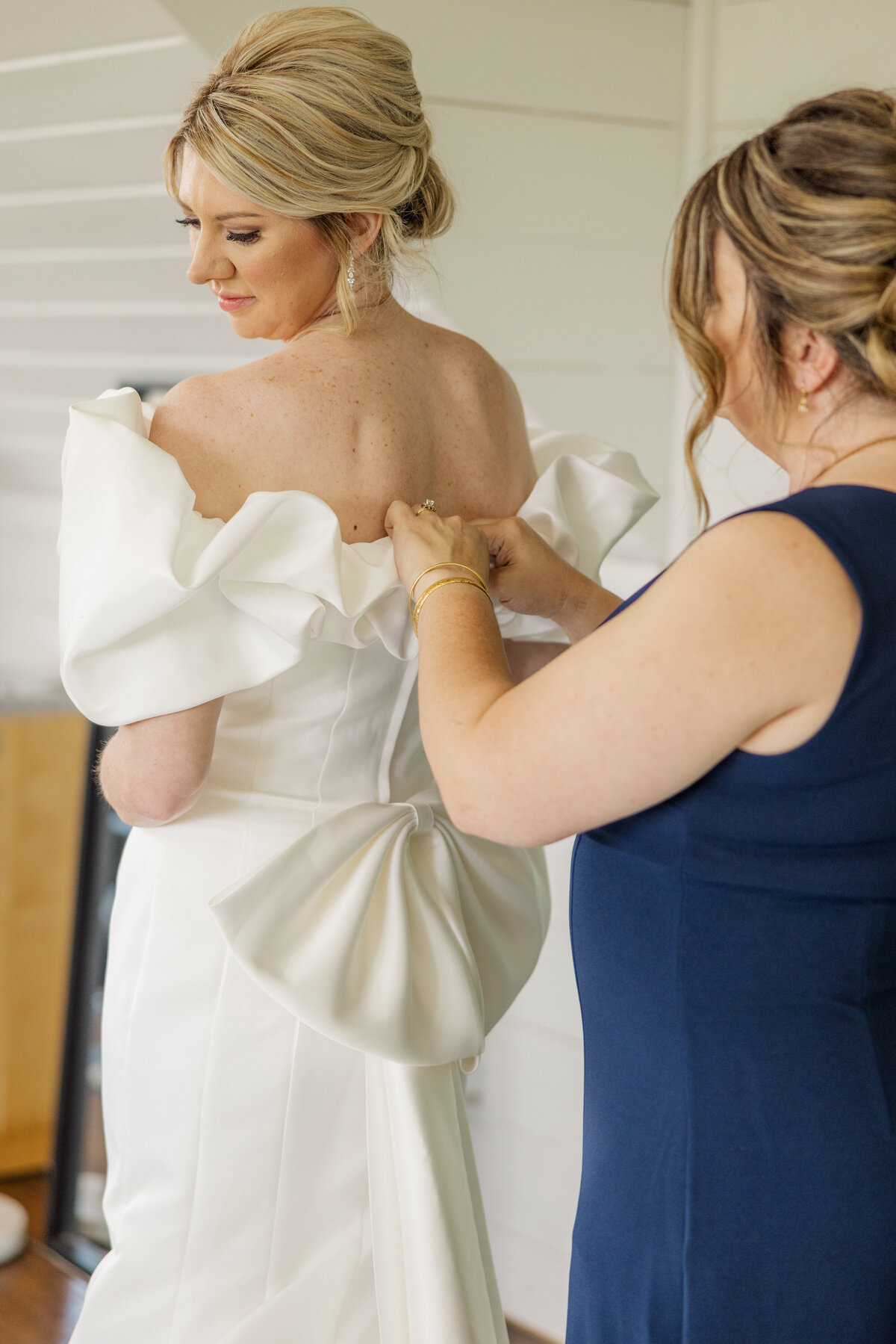 Mom fastens up bride in her elegant ruffled dress with large bow on the back. 