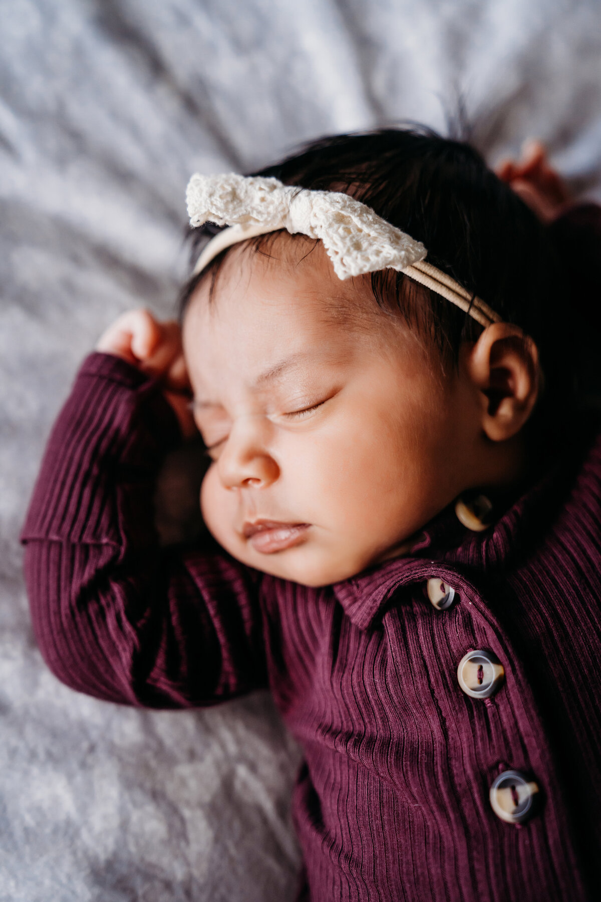 Newborn Photographer, a baby girl sleeps on her bed with a bow in her hair