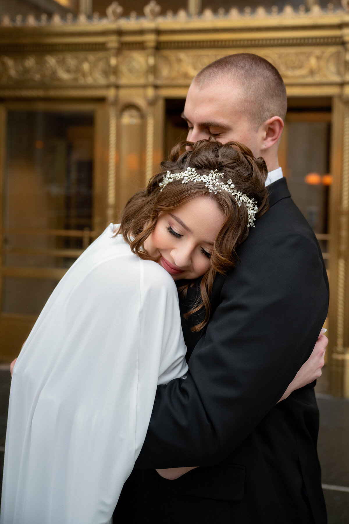 short hair brunette bride with tiara is leaning on her husband's shoulder with her eyes closed 