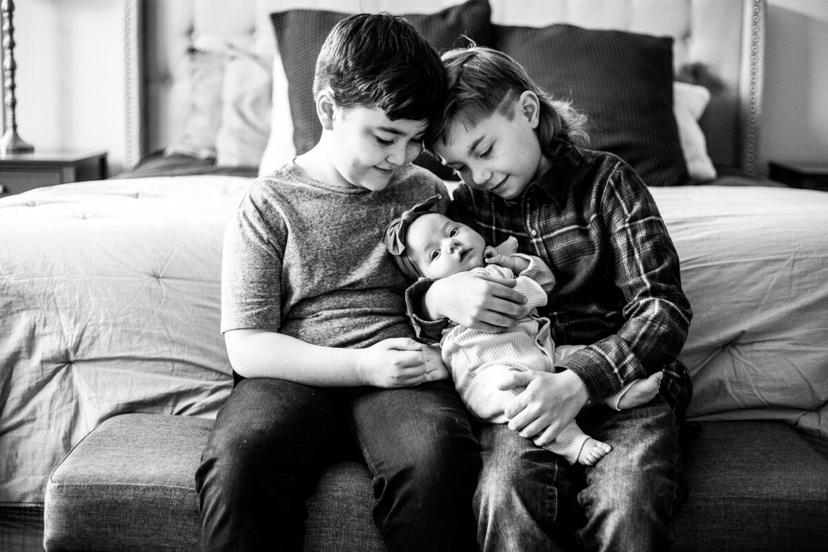 Black and white photo by portland oregon newborn photographer of siblings and newborn baby at the end of bed in primary bedroom.