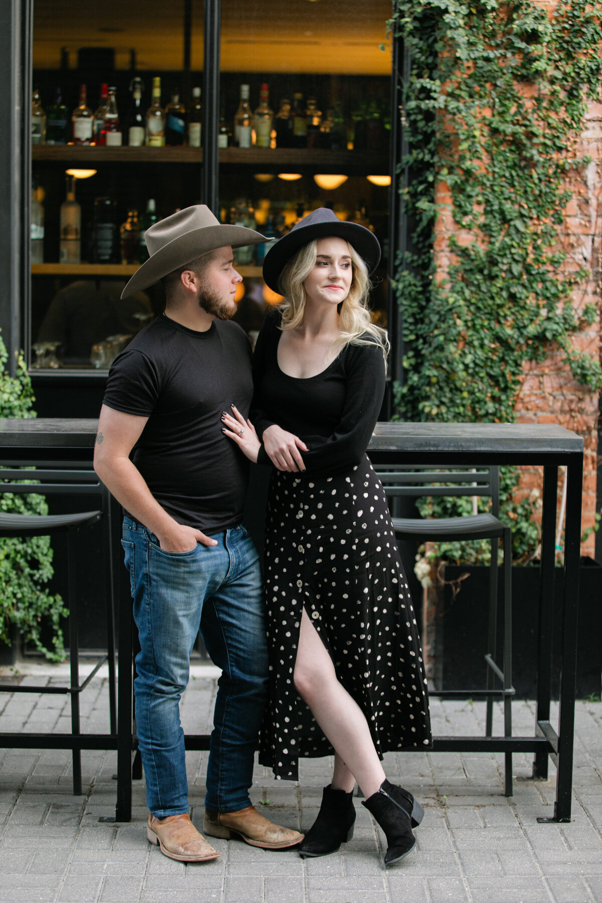 Couple in Deep Ellum, Dallas during their engagement session, both wearing cowboy hats and looking stylish.