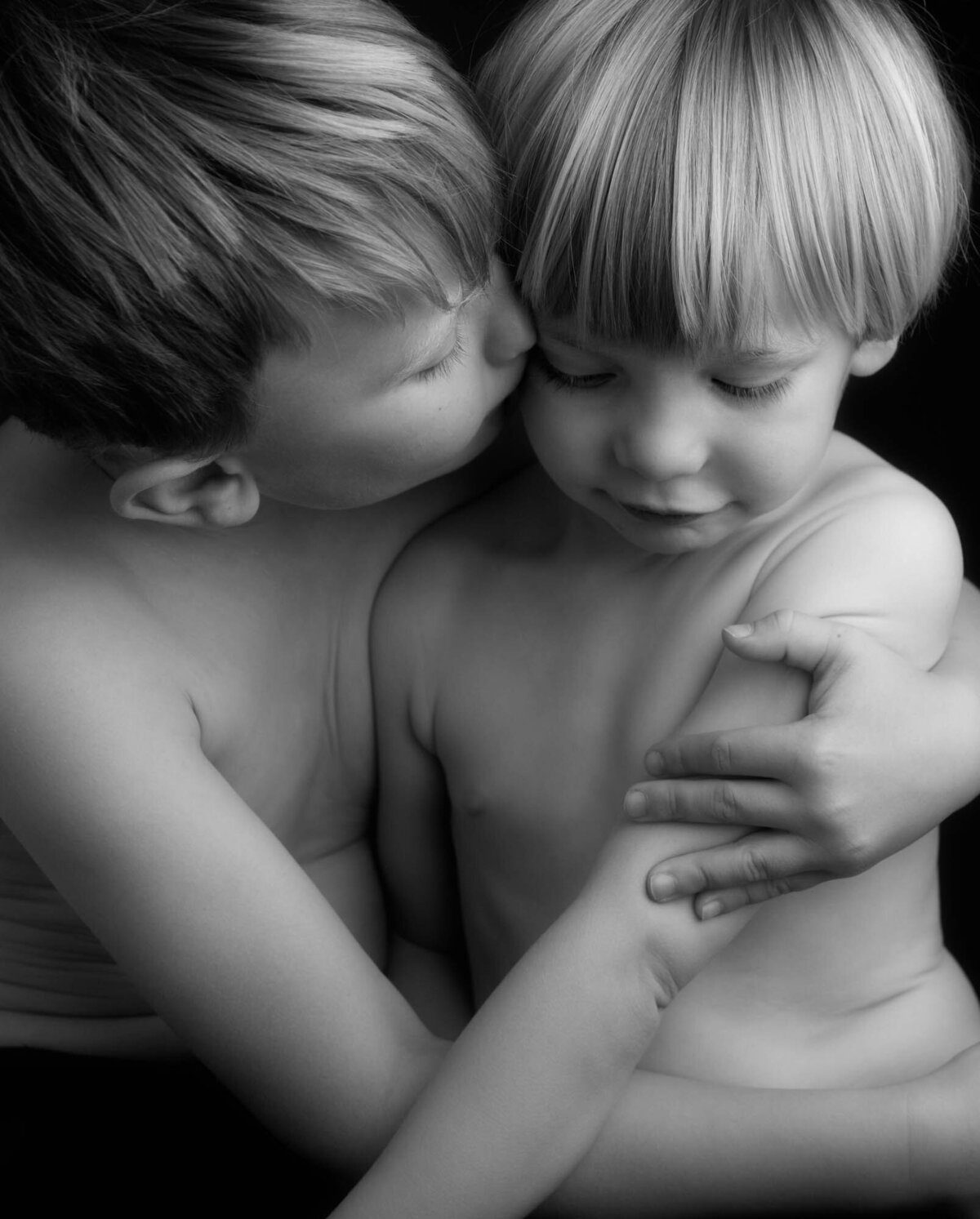 Two boys sharing a kiss in a pop-up photography studio against a striking black background.