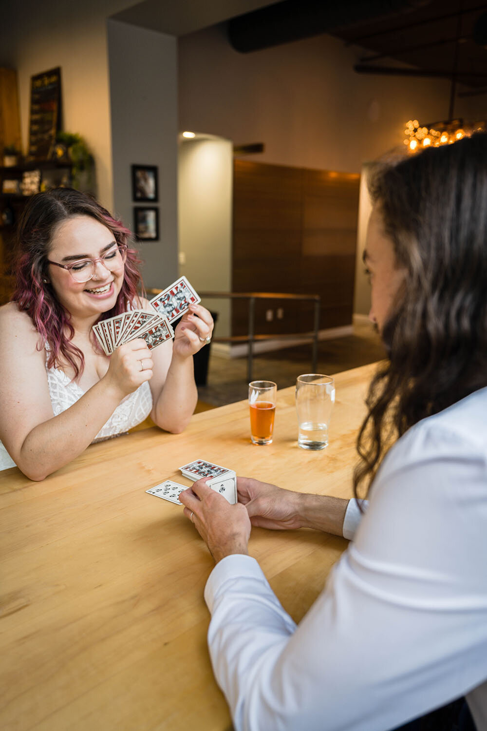 A newlywed spouse sits across from her significant other and smiles at her deck of cards during a card game they started to play during their elopement in Downtown Roanoke at Olde Salem Brewery.