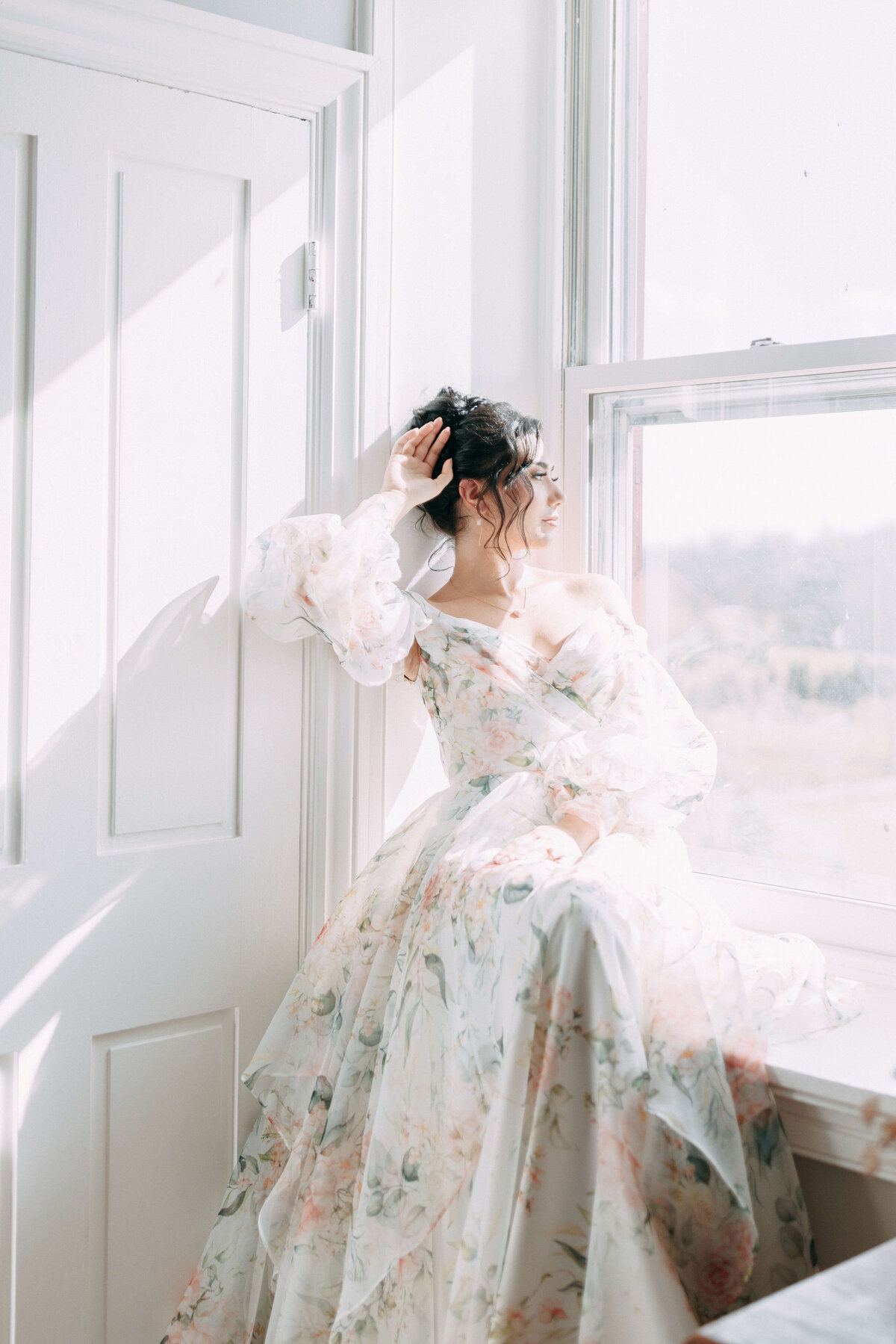 bride in floral wedding dress sitting by window