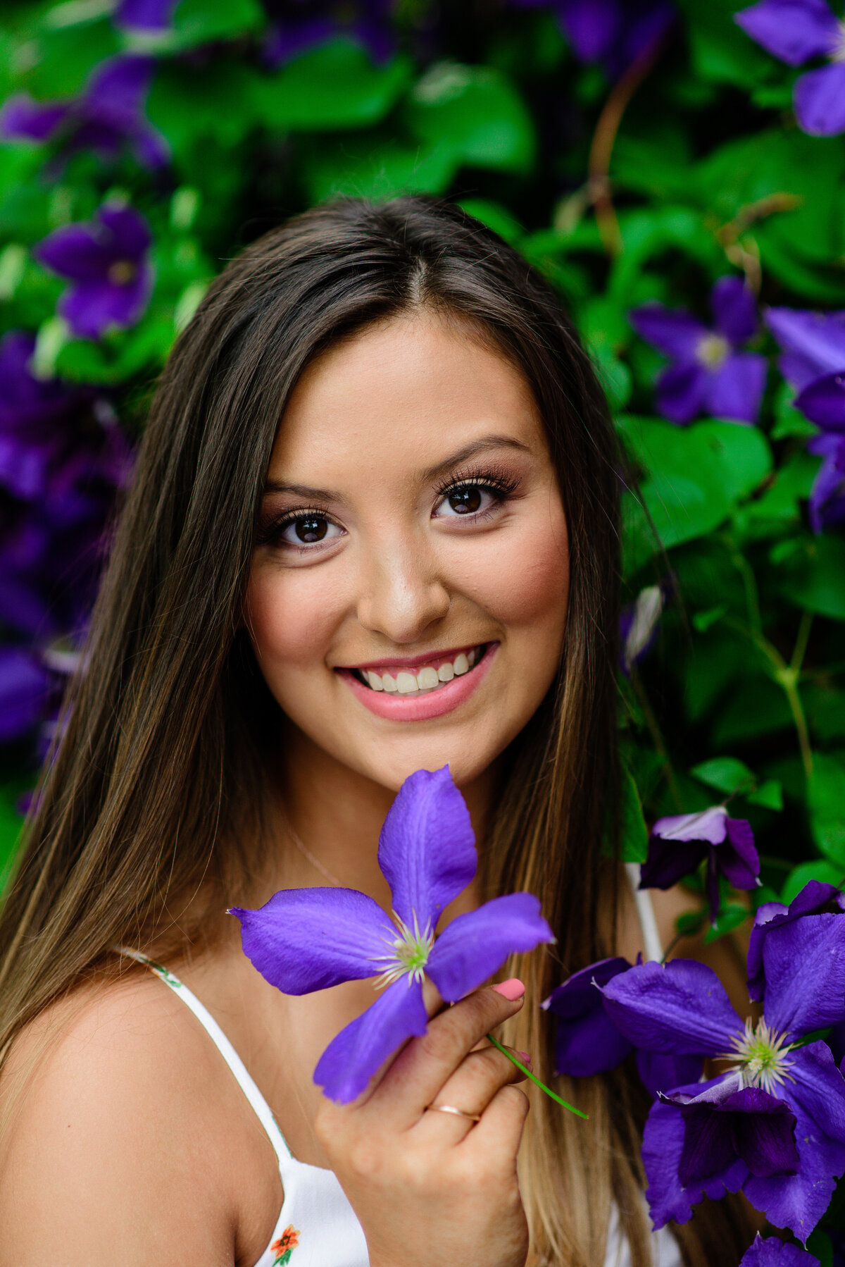 senior photos denver with girl posing with purple florals in a bush as she smiles and holds the flower to her face photographed by denver senior photographer