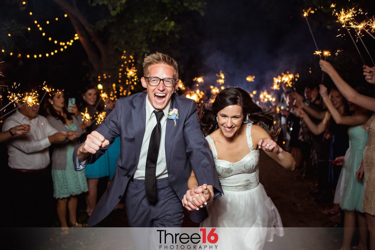 Bride and Groom exit the reception by running under a tunnel of sparklers being held by wedding guests