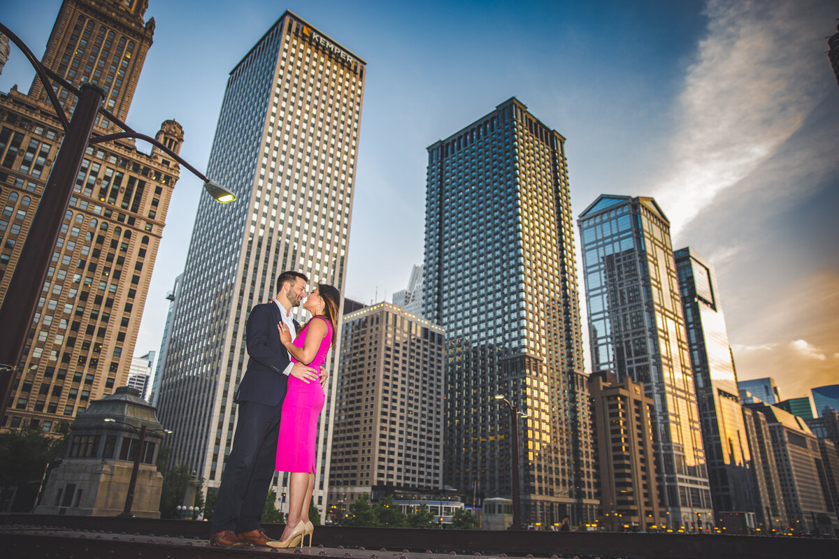 An engagement photo of a couple standing on a bridge against the skyline of Chicago