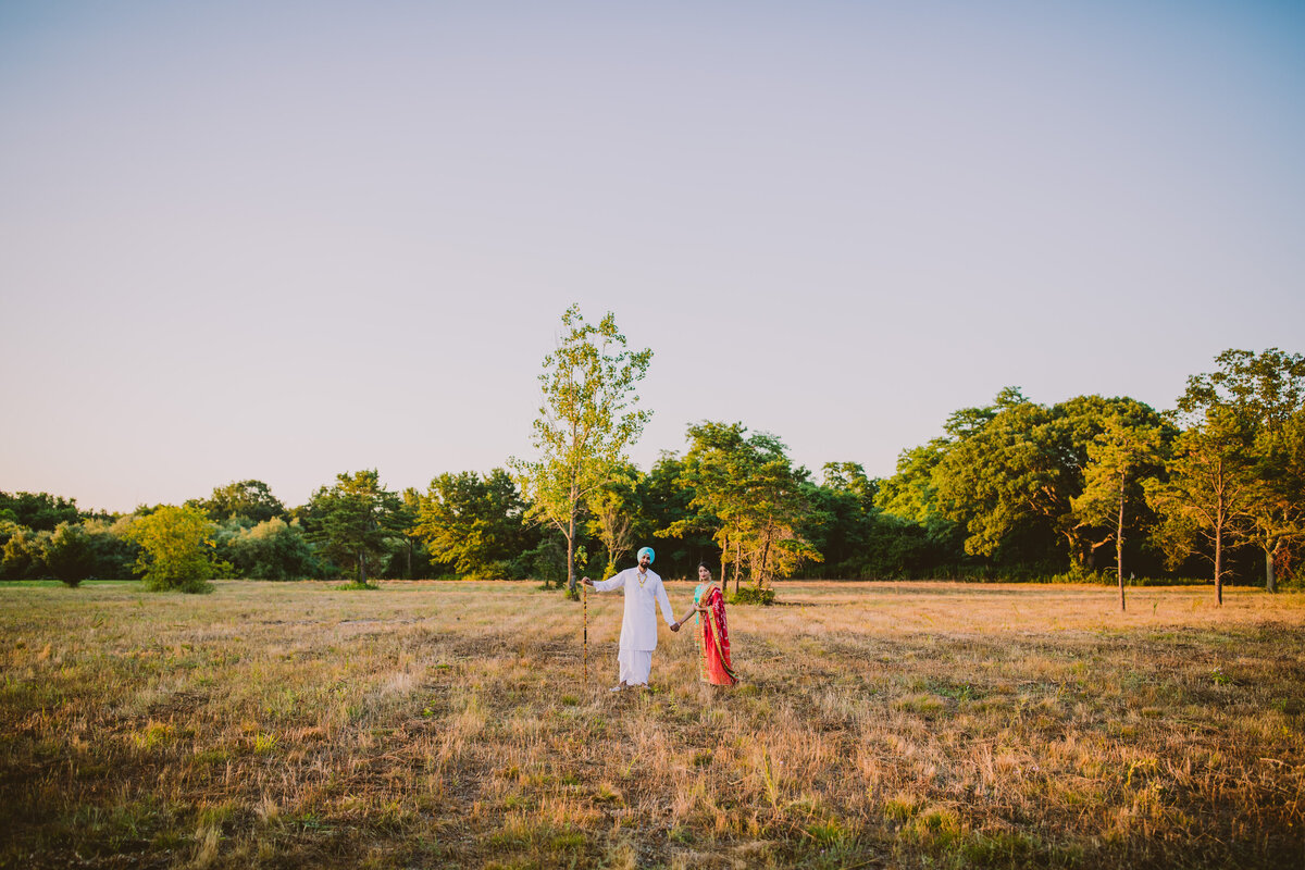 A far away shot of a bride and groom standing in the middle of a field in traditional punjabi clothing for their engagement shoot in long island