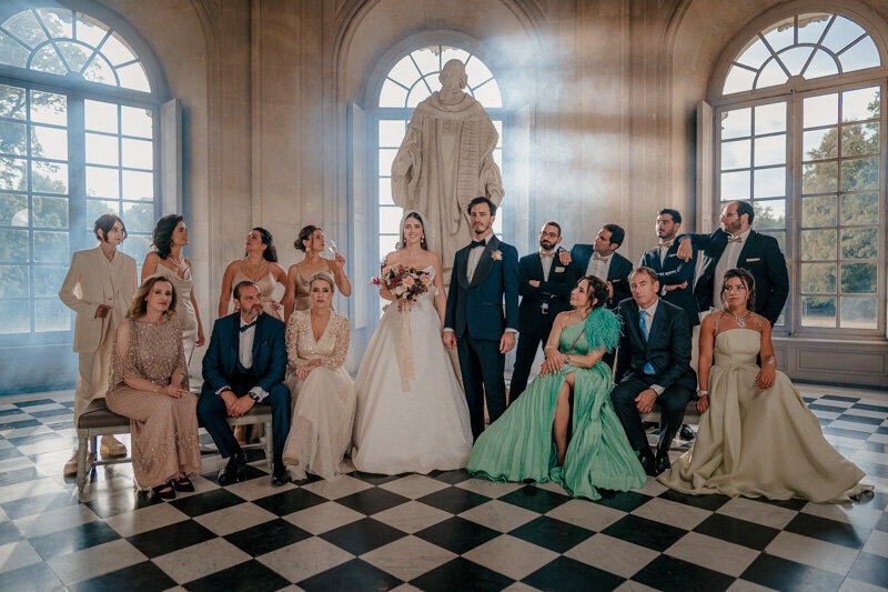 Photo de groupe chic et stylisée façon Vanity Fair au Château de Champlâtreux, avec les mariés entourés de leurs proches dans un décor élégant et théâtral.
