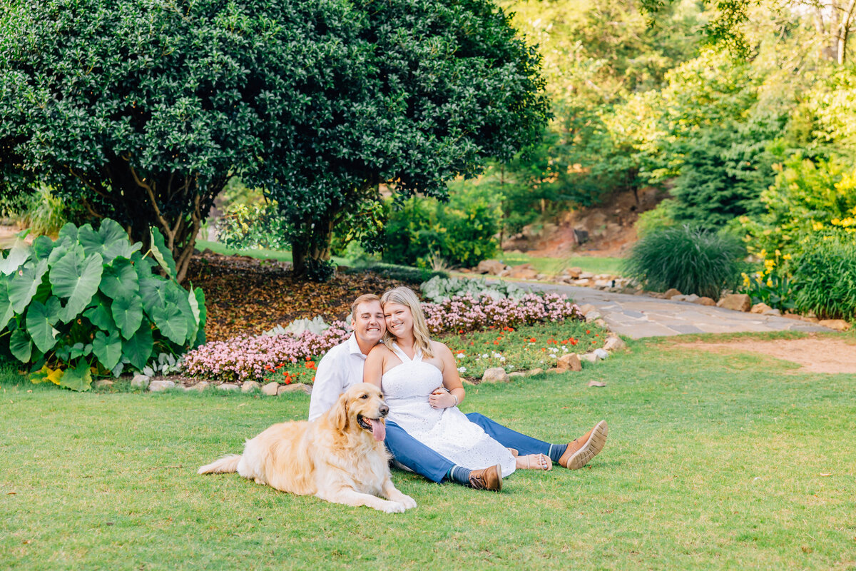 couple sitting on green grass for engagements with their golden retriever in greenville, south carolina