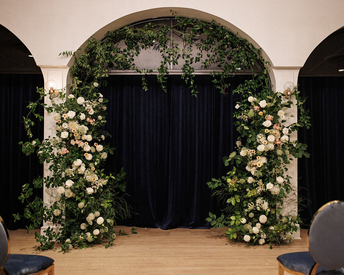 A floral wedding ceremony arch at the Atwater Club features lush white flowers and suspended greenery.