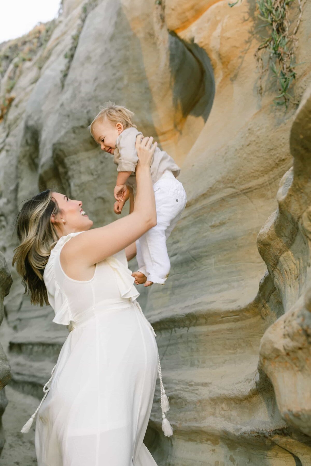 Orange County Maternity Photographer. - pregnant mother in a white dress holding up her baby with joy