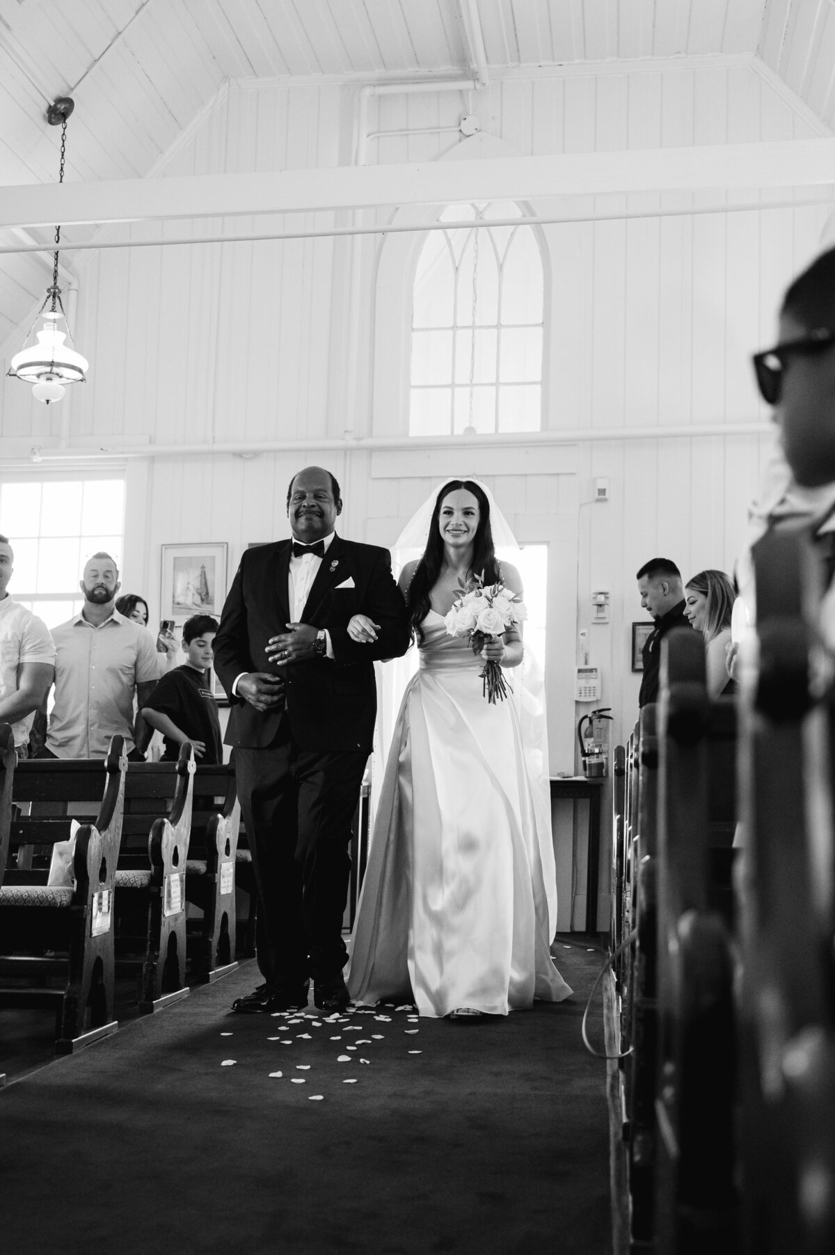 father of the bride  walking her up aisle of church in black and white