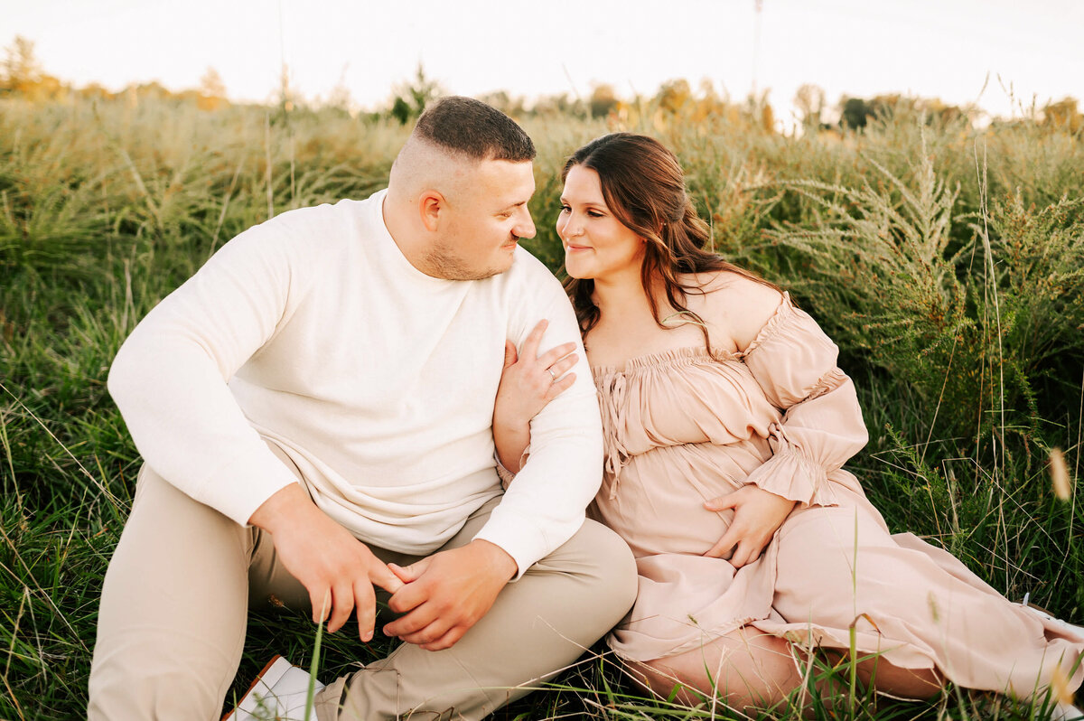 maternity photo in Joplin MO of pregnant couple smiling at each other sitting in grass