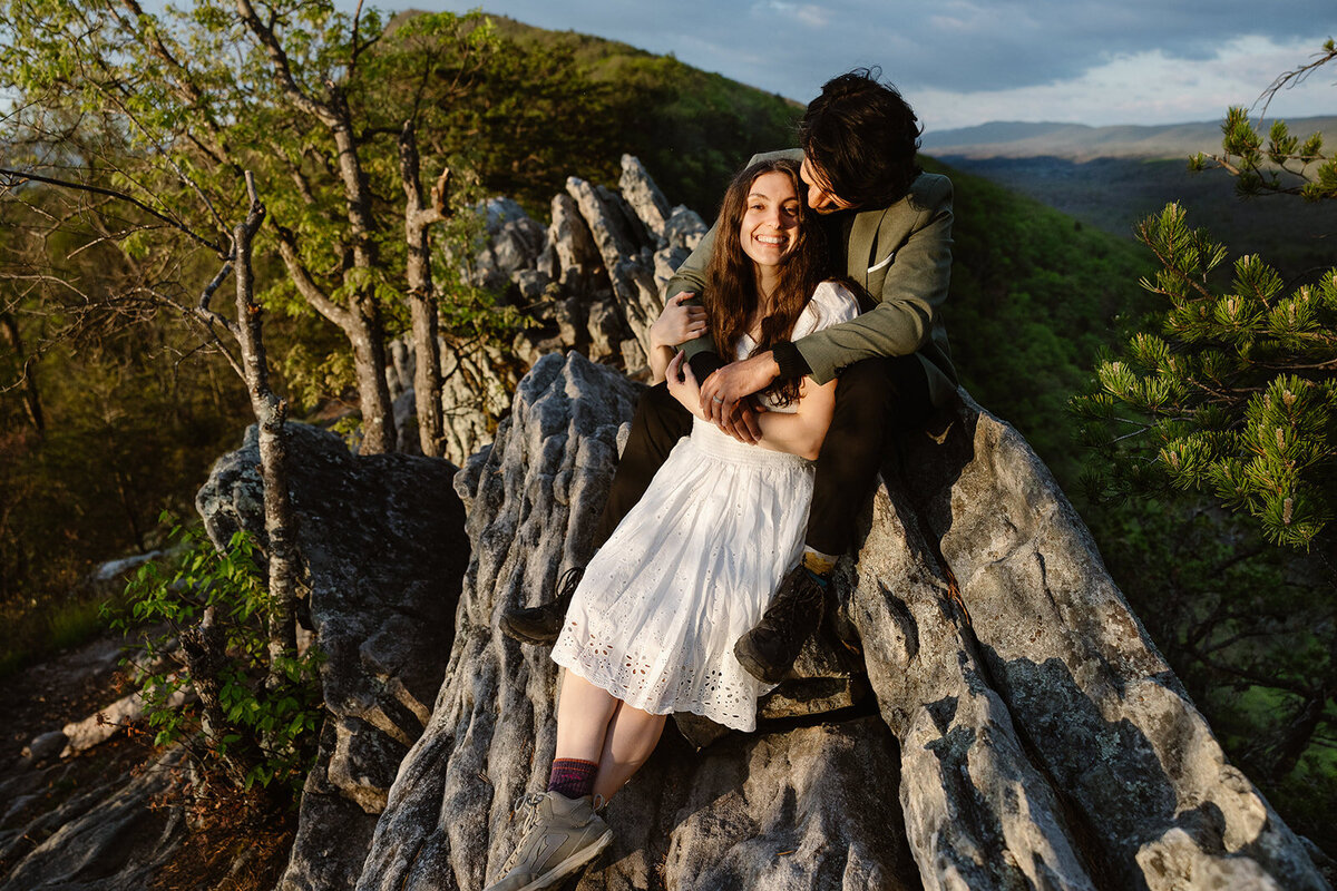 A couple sits atop Buzzard Rock outside of Shenandoah. They are snuggled up, and they both wore hiking boots on their elopement day