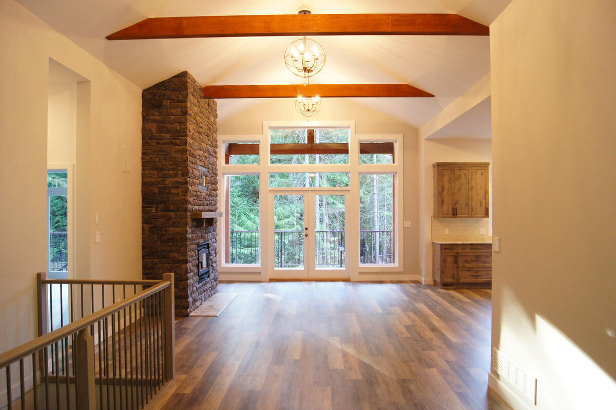 Open concept living room with stone fireplace and wood ceiling beams.