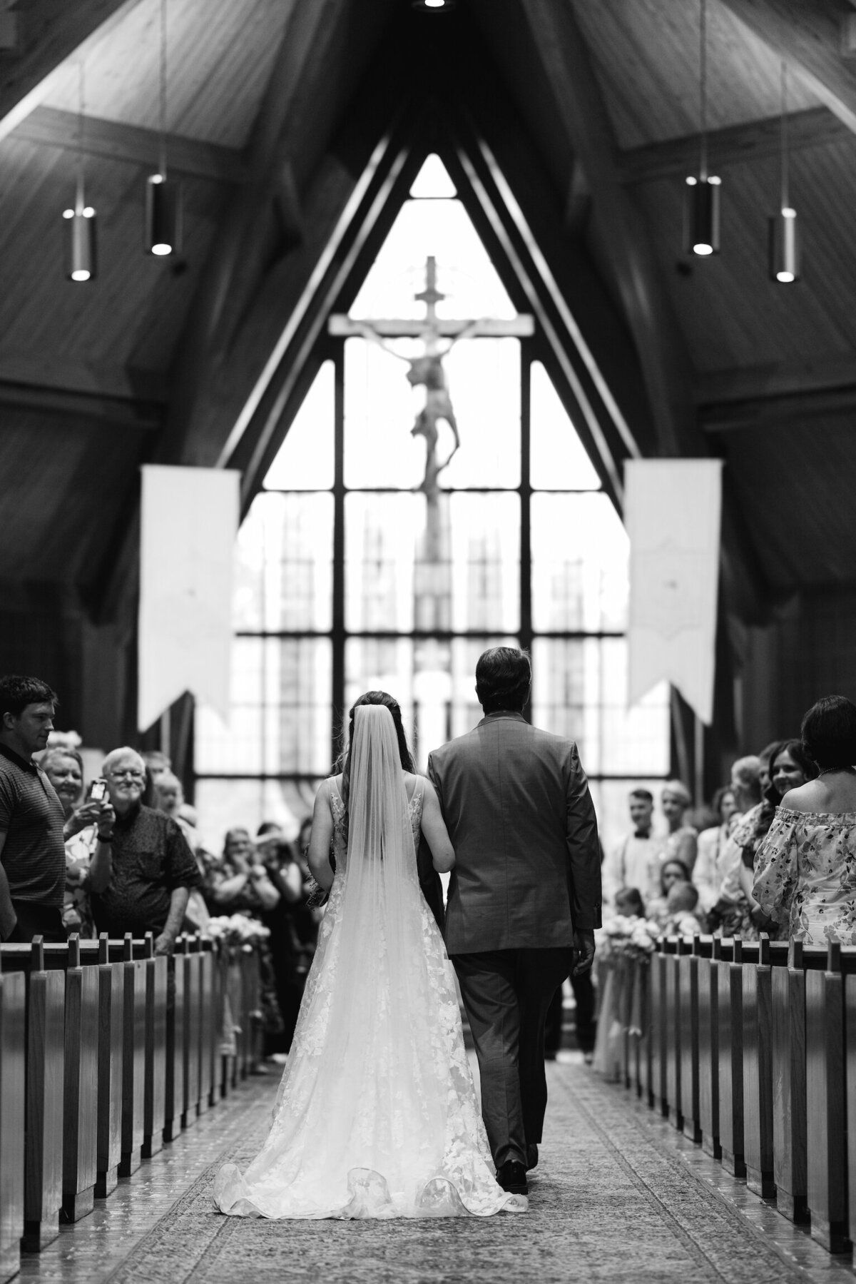 A timeless black-and-white capture of the bride and her father walking down the aisle, filled with emotion and tradition, beautifully documented on film by Morgan Alysse, Louisiana film photographer.