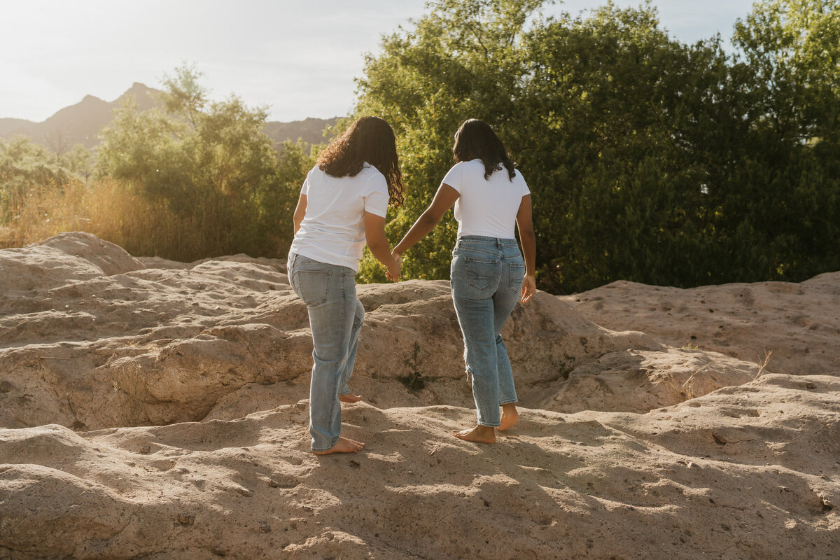 A couple holding hands and walking along rocks together 