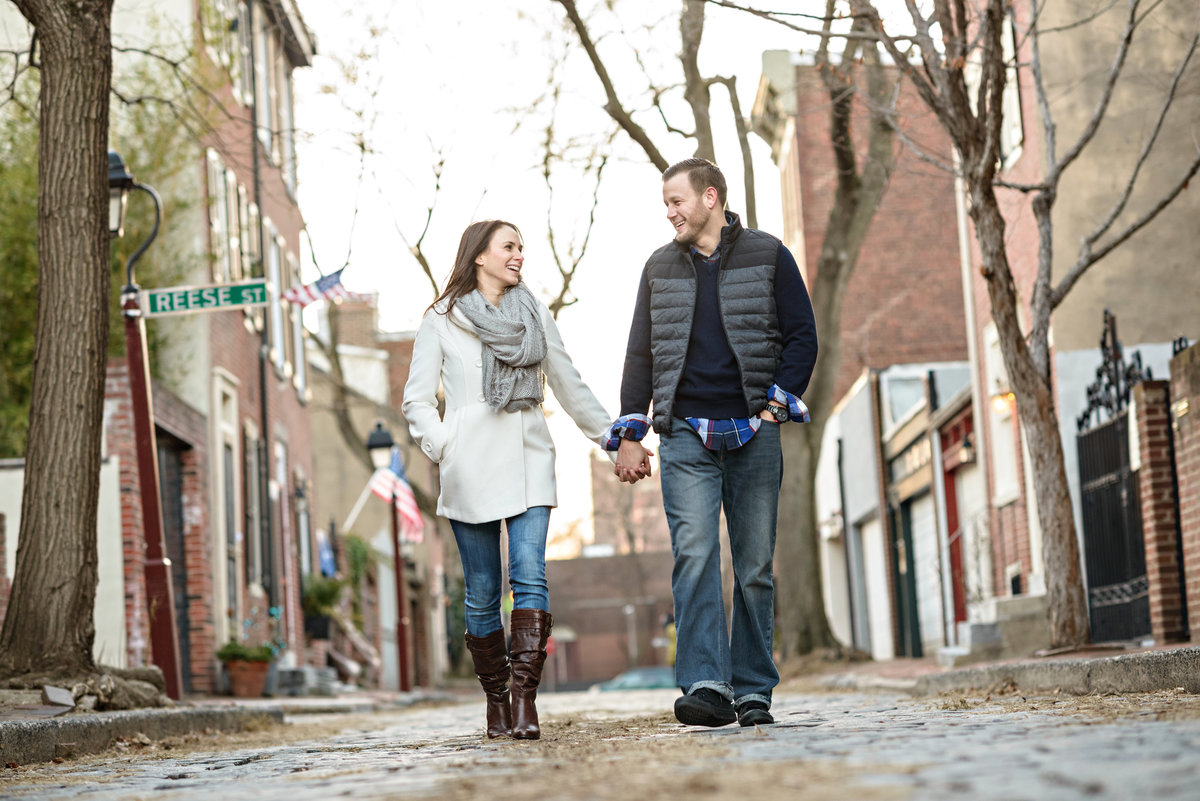 Two engaged people walk the cobblestone streets of old city philadelphia.