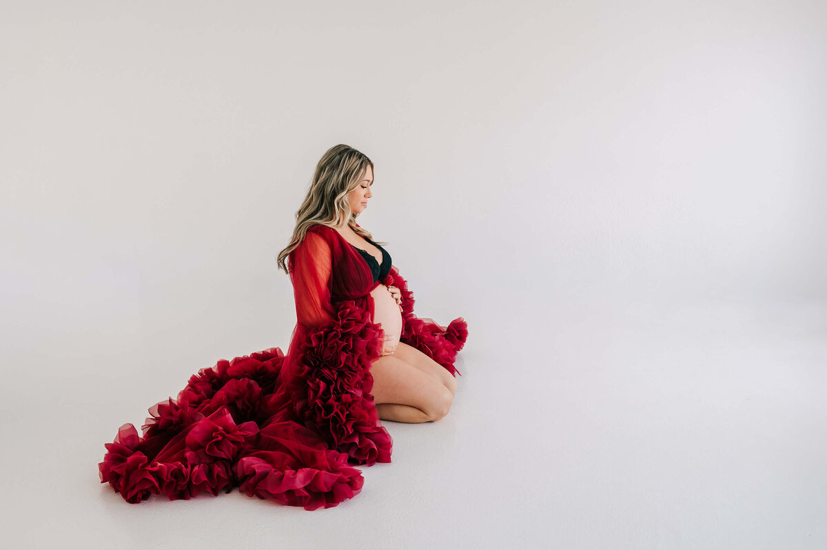 pregnant mom kneeling on floor holding baby bump during Joplin MO maternity photography session