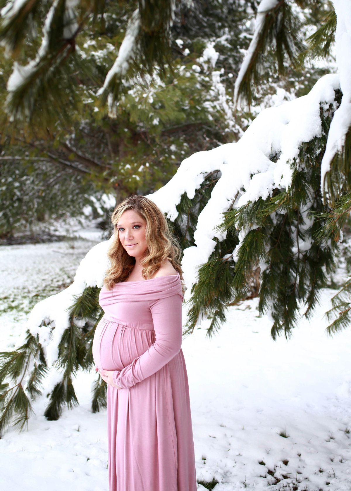 pregant woman with blonde hair in light pink maternity gown against snowy scenery
