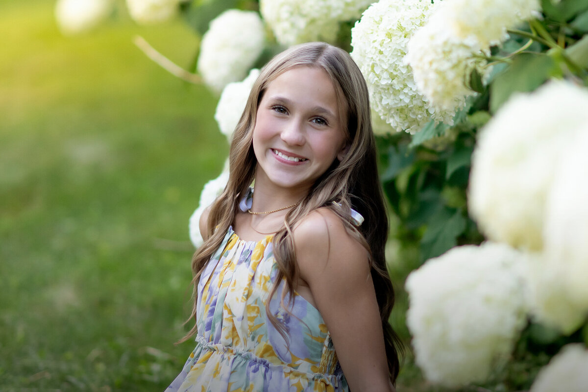 A little girl smiles big for her photo in front of big white flowers