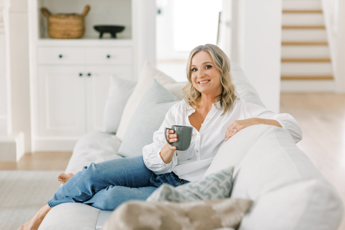 Top Windsor, ON Interior Decorator Jen Sottosanti arranges greenery in her luxury living room. Behind her is a oversized mantle and wood built-ins.