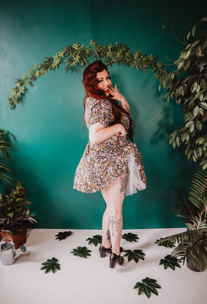 Pinup woman with red hair and floral dress surrounded by green plants