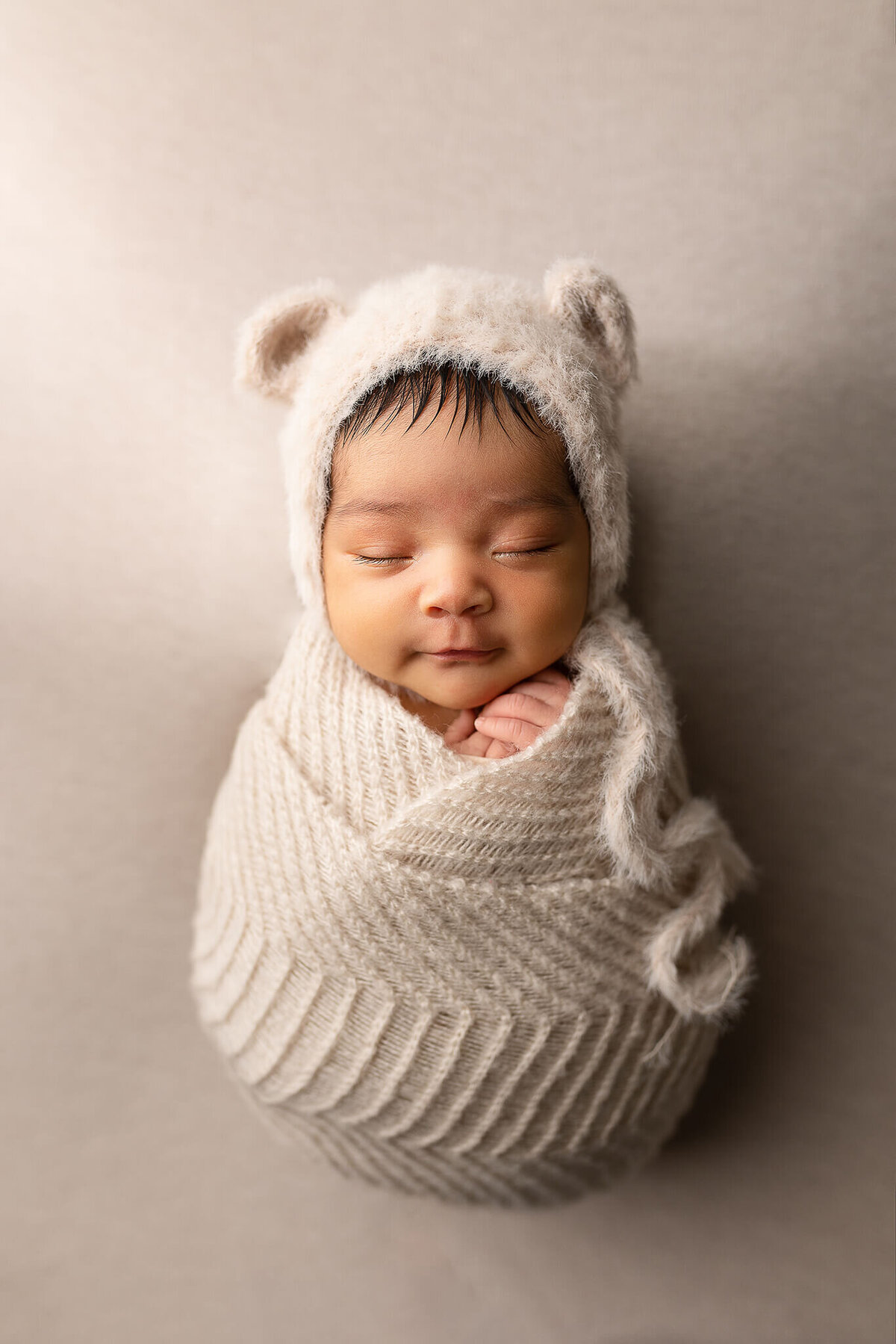 Newborn boy wearing a fuzzy bear bonnet.