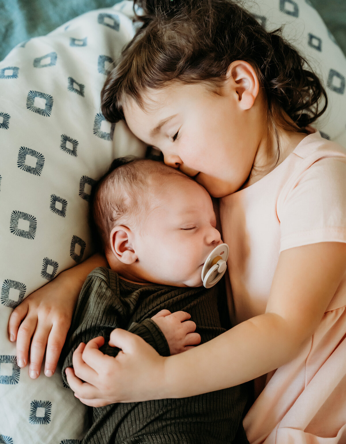Newborn Photographer, a little girl snuggles with her baby brother as they sleep in the crib