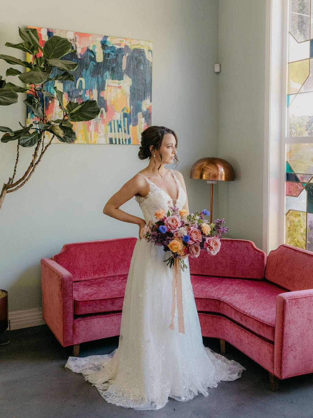 Bride holding a colorful bouquet in front of a pink couch