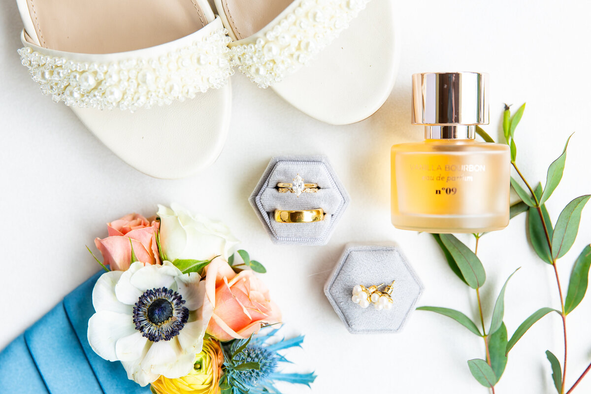 Brides shoes, grooms bouquet and greenery next to their rings