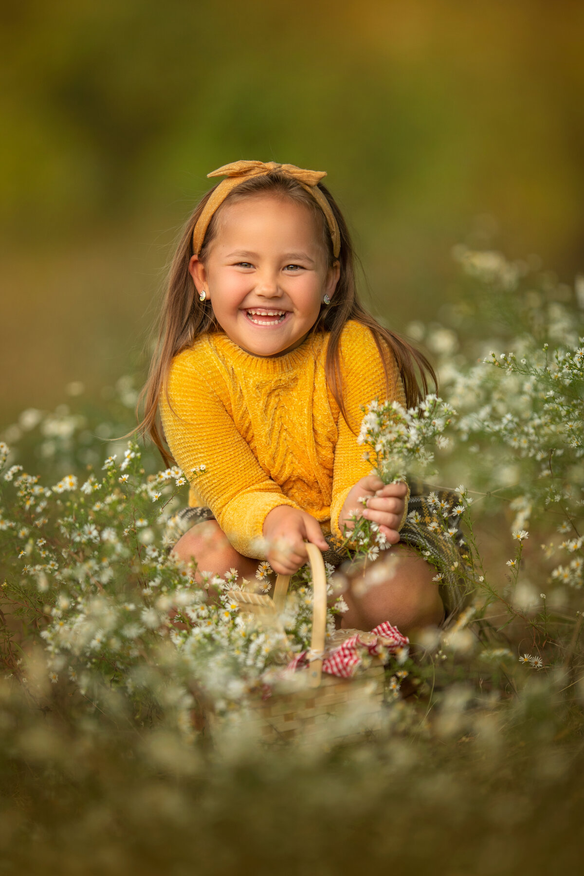 girl with a big smile is picking daisies in the fall in mustard color outfit and headband.
