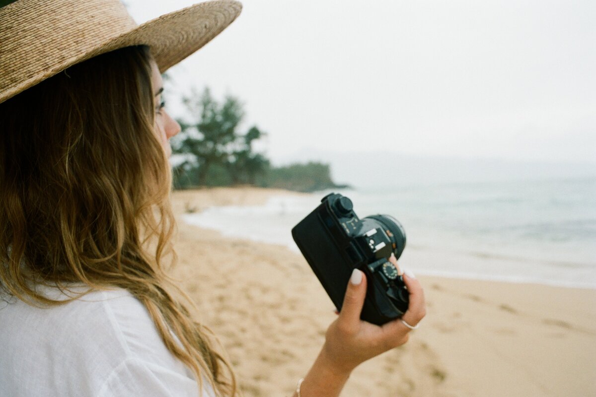 Girl with a film camera at the beach captured by Kate Winters Photography, showcasing a candid and nostalgic moment in an authentic, documentary style.