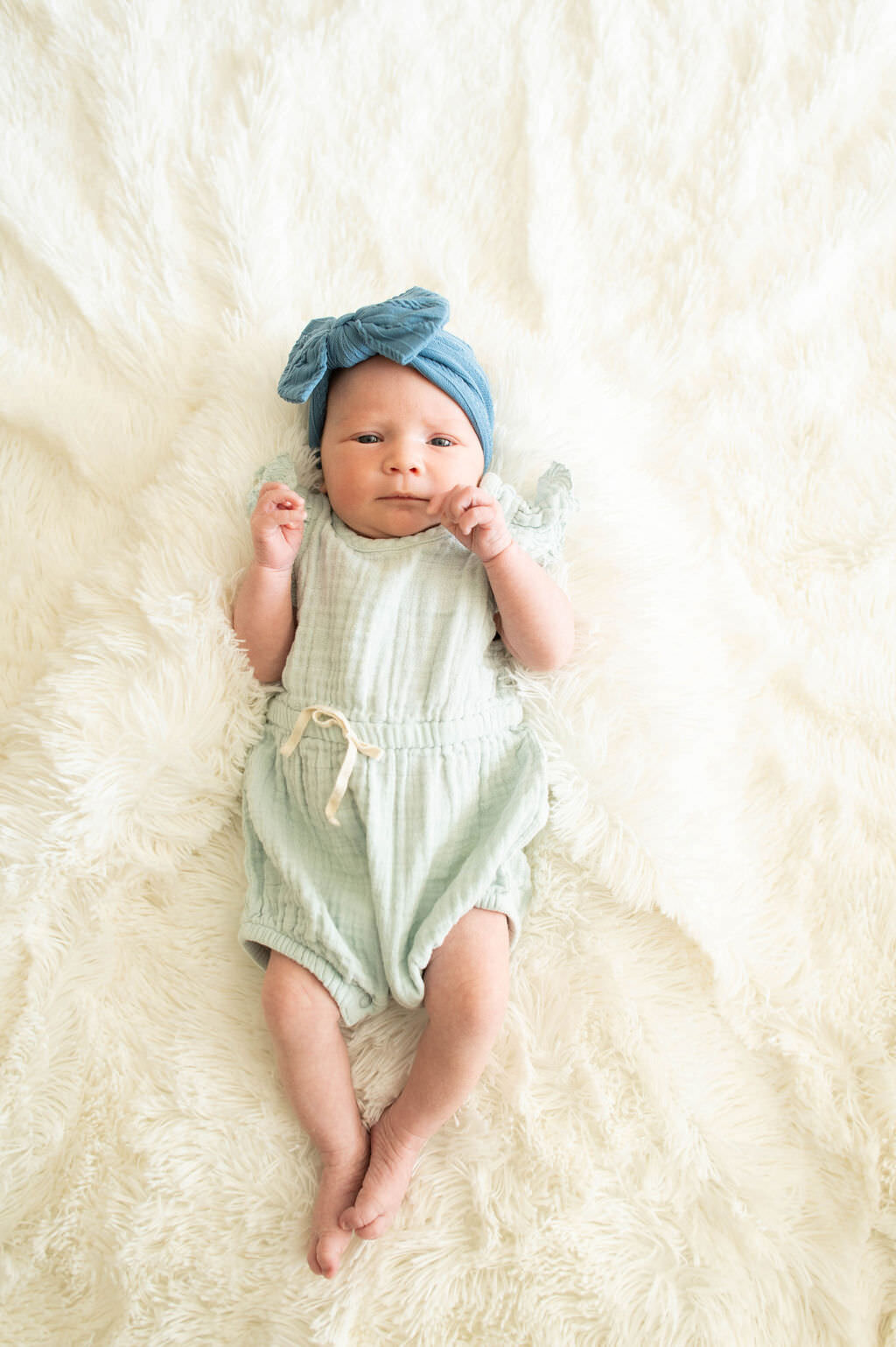 A newborn baby in a blue bow laying on a white blanket.