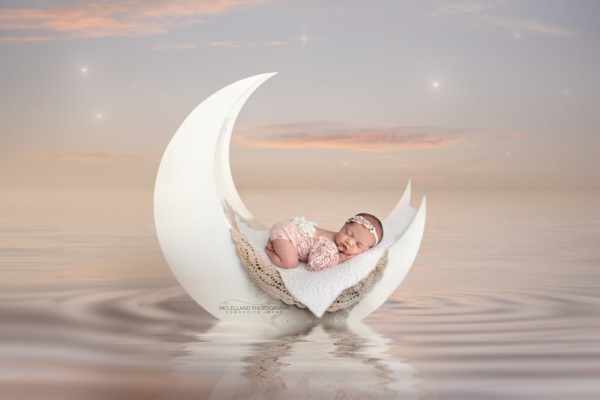 Newborn in a crescent moon prop hovering above soft misty clouds