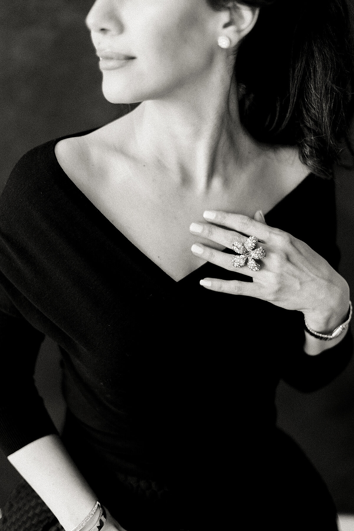 An elegant black and white boudoir photo of a woman wearing a black dress and she delicately touches her chest while posing in a Dallas photography studio.